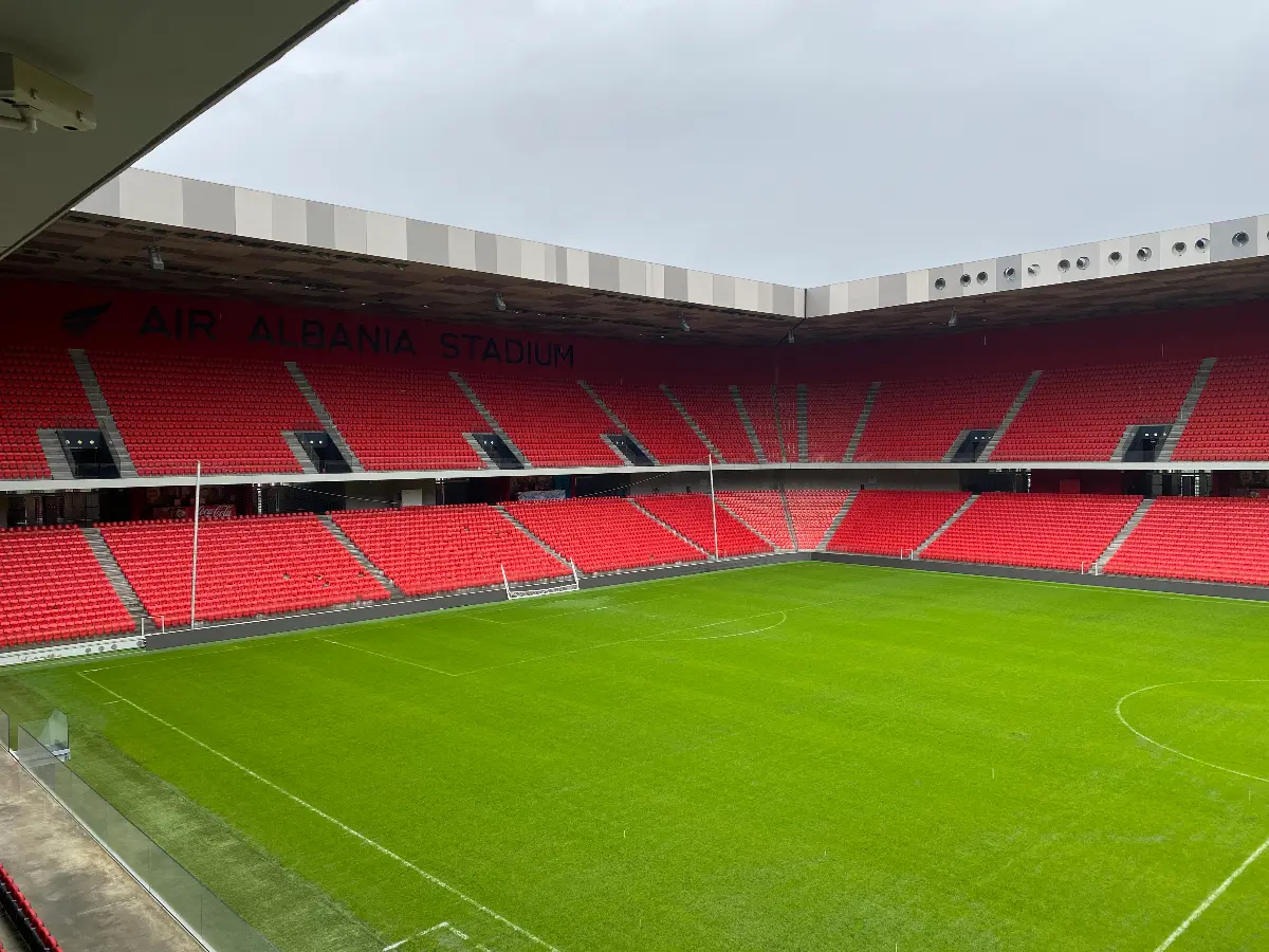 Interieur van het Air Albania Stadion met rood gestoffeerde zitplaatsen en een groen speelveld, gezien vanaf een van de tribunes.