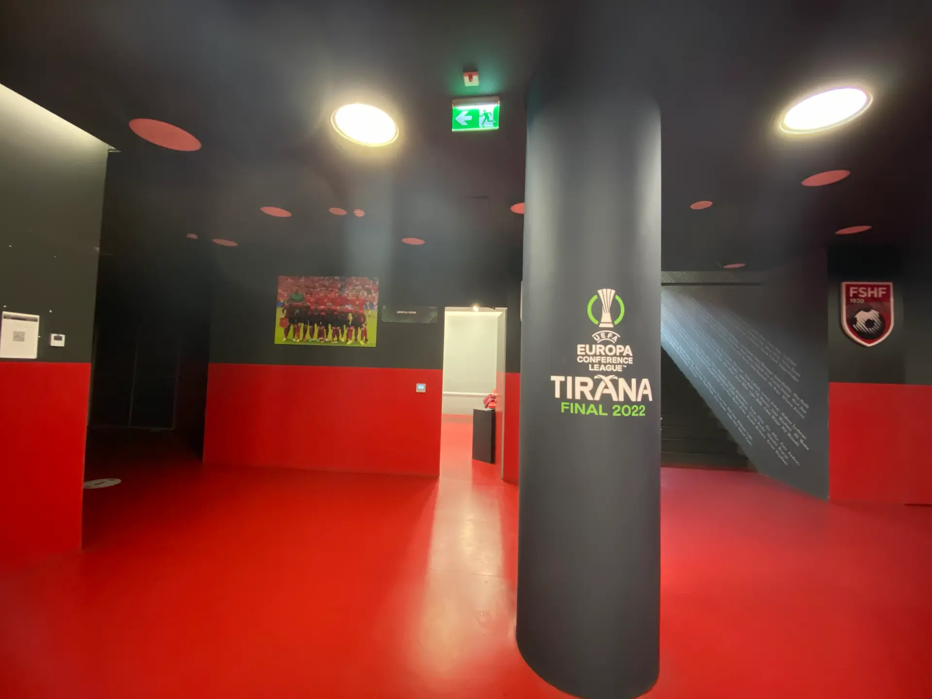 Een ruimte met rood/zwarte muren en een rode vloer uitkijkend op een zwarte pilaar met een groen/wit logo erop.