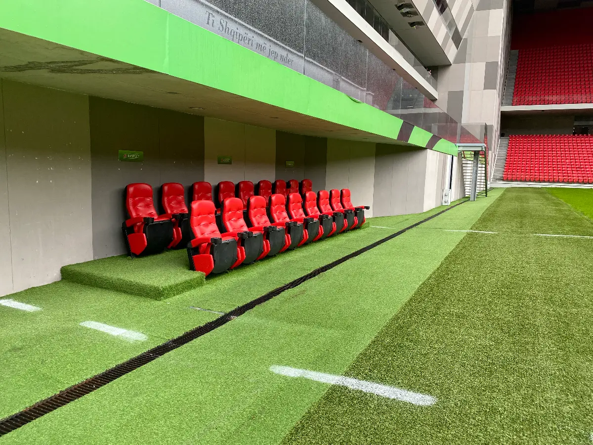 Een rij rode stoelen in het Air Albania Stadion met groen gras.
