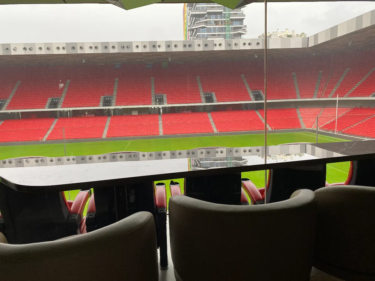 Een bar met een tafel in het Air Albania Stadion, uitkijkend op het groene speelveld en rode tribunes.