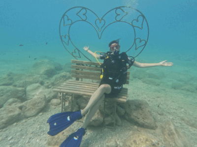 diving in albania Duikster poseert lachend op een bankje onder water