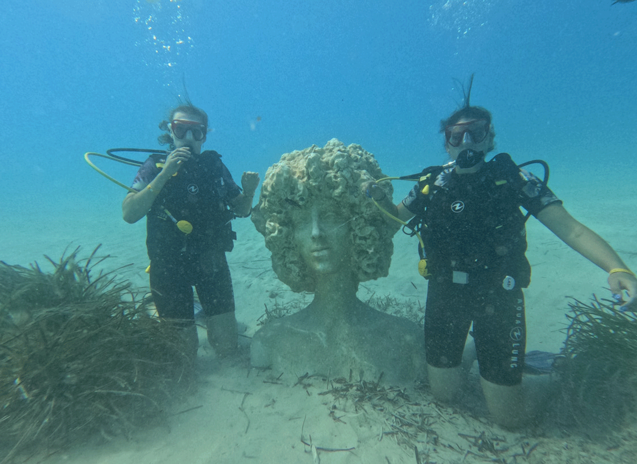 Twee duiksters poseren bij een onderwaterbeeld