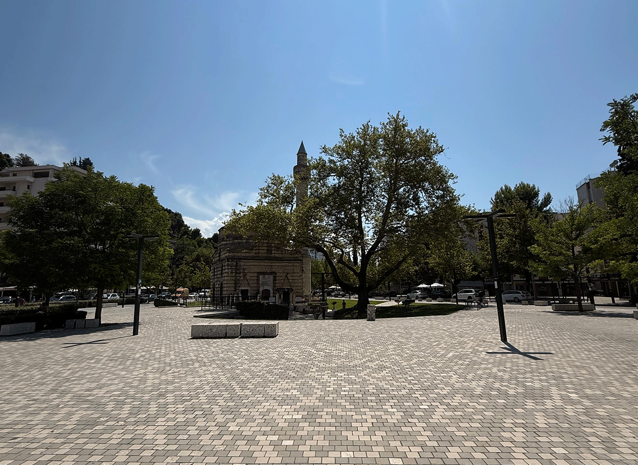Open plein met oude Muradie-moskee en schaduwrijke bomen eromheen.