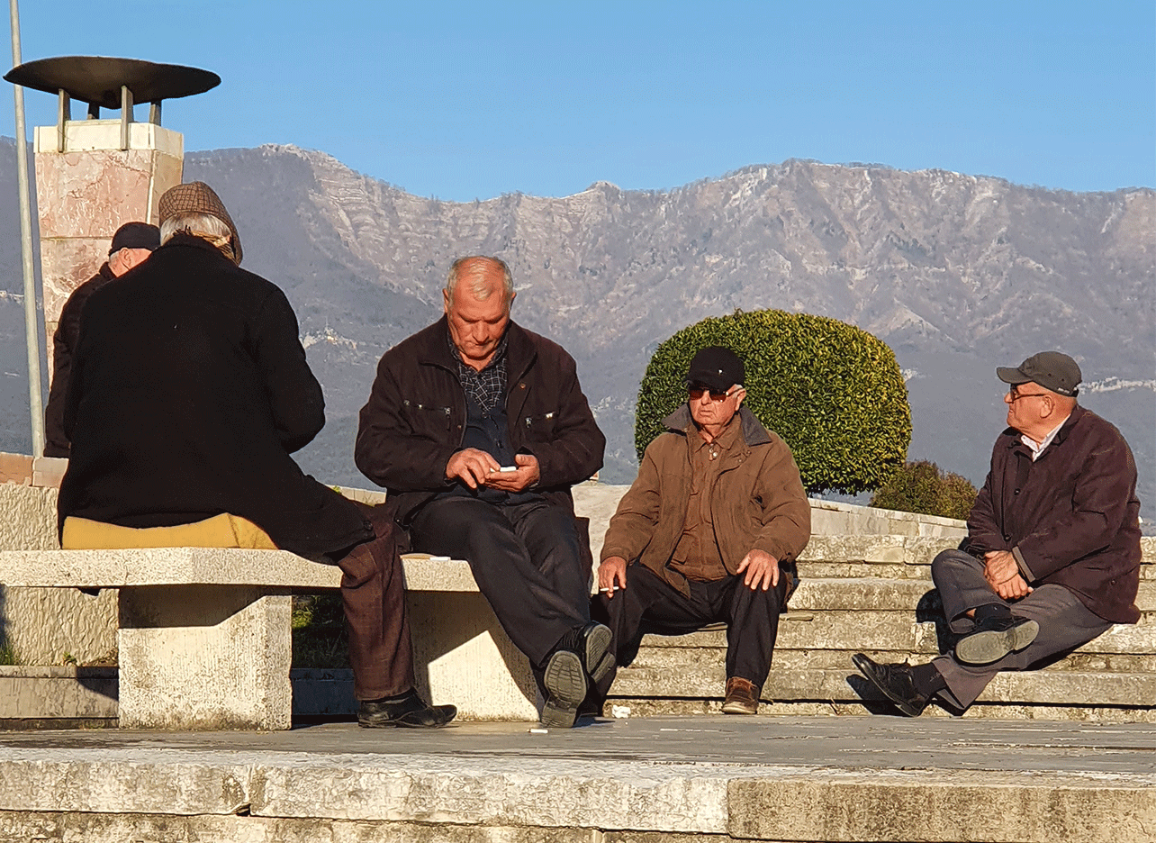 Een groep oudere mannen zit op een bank in het park en praat in de zon.