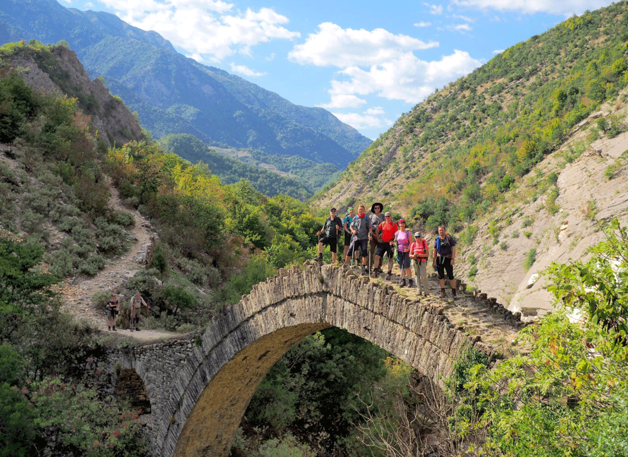 Groep wandelaars die een Ottomaanse stenen brug oversteken in de Zagoria-vallei.