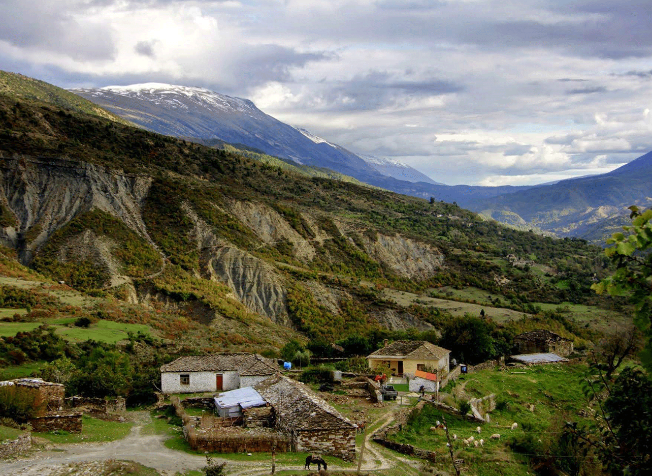 Uitzicht op een klein dorp in Zagoria, omringd door bergen en velden.