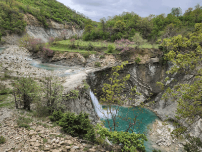 ZAGORIA-HIDDEN-VALLEY-TREK Waterval en turquoise rivier in de Zagoria-vallei, omgeven door lentegroen.